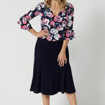 Full body shot of 40 year old woman wearing a 3/4 sleeved shirt with a rose print design. Patterned & easy care fabric made of dry touch jersey fabric. Work wear shirt is navy with pink and white roses. This breathable shirt is Australian made. Made by woman in Australia and NZ. Leina & Fleur is a woman’s clothing brand that proudly stocks sizes from 8 to 24 including petite & plus sizes.
