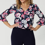 Close up view of forty year old woman wearing a 3/4 short sleeved top. Top has a V neck shape and is made of dry touch jersey material. Blouse has a floral design with roses in the colours pink, white and navy. Easy care fabric is Australian made by women in Australia and New Zealand. Woman’s clothing retailer Leina and Fleur stock petite and plus sizes from 8 to 24.