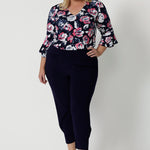 Full body view of plus sized woman. Wearing a 3/4 sleeved shirt with a floral pattern. Made of high quality dry touch jersey fabric. Work wear shirt has pink and white roses on a navy coloured base. This shirt is breathable, easy to care for and Australian made. Made by woman in Australia and New Zealand. Leina and Fleur is an online woman’s clothing brand that has sizes from 8 to 24 including petite & plus sizes.