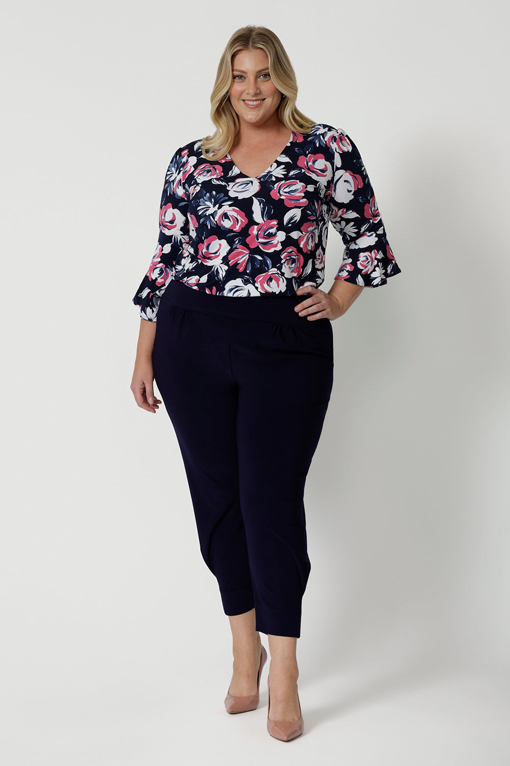 Full body view of plus sized woman. Wearing a 3/4 sleeved shirt with a floral pattern. Made of high quality dry touch jersey fabric. Work wear shirt has pink and white roses on a navy coloured base. This shirt is breathable, easy to care for and Australian made. Made by woman in Australia and New Zealand. Leina and Fleur is an online woman’s clothing brand that has sizes from 8 to 24 including petite & plus sizes.