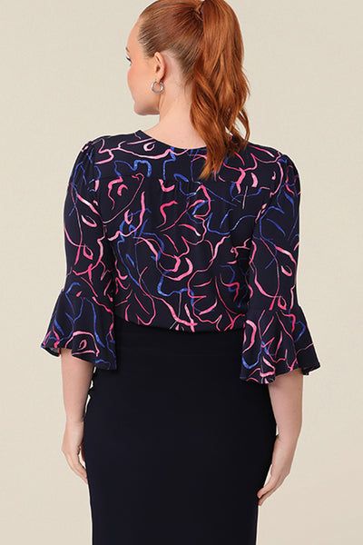 Back view of a women's workwear top in pink and blue abstract print. Featuring a V neckline and 3/4 sleeves with fluted cuffs, this top is made in Australia for petite to plus size women,