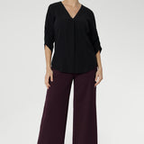This shirt features a V-neckline with a tailored tuck at the front for a polished look. The back neckline is finished with a facing and a soft pleat that adds subtle detail. The 3/4 length sleeves include elegant ruching that falls toward the centre front of the arm for a refined finish.
