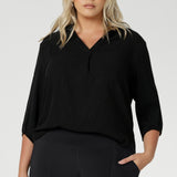 Plus size woman wears Graphite coloured woven shirt with collar and tailored pleat with navy workwear pants and black heels for an elevated corporate look. Made from sustainable Tencel fabric in Australia for petite and plus size woman sizes 8-24. 