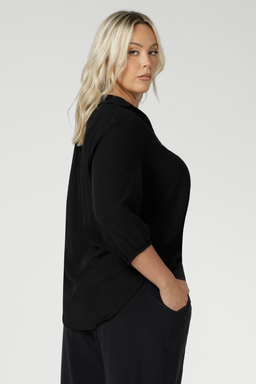 Side view of plus sized woman wears Graphite coloured woven shirt with collar and tailored pleat with navy workwear pants and black heels for an elevated corporate look. Made from sustainable Tencel fabric in Australia for petite and plus size woman sizes 8-24. 