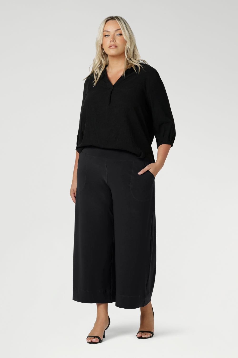 Plus size woman wears Graphite coloured woven shirt with collar and tailored pleat with charcoal workwear pants and black heels for an elevated corporate look. Made from sustainable Tencel fabric in Australia for petite and plus size woman sizes 8-24. 