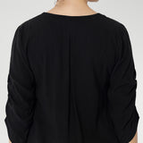 The back neckline is finished with a facing and a soft pleat that adds subtle detail. The 3/4 length sleeves include elegant ruching that falls toward the centre front of the arm for a refined finish.