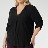 Plus size woman wears 3/4 length sleeve top with elegant ruching details that falls toward the centre front of the arm for a refined finish. She's styled her Terry Shirt in Graphite with wine coloured pants. 