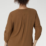 The back is finished with a subtle pleat for a touch of structure and flow. With beautifully ruched ¾ sleeves that fall gracefully toward the front of the arm.