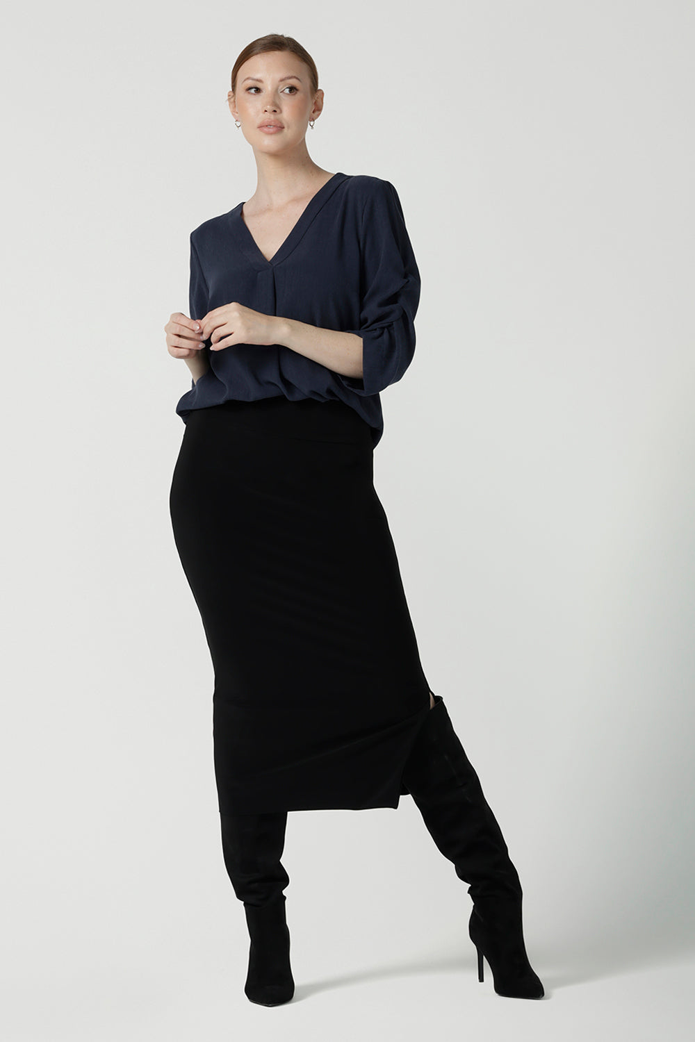 A size 10 woman wears the Terry Top in Bluestone, a Navy tencel shirt that is breathable and soft. Made in high quality fabric in Australia. Soft V-neckline and ruched sleeves. Made in Australia for women size 8-24. Styled back with the Andi Midi tube skirt in black. 