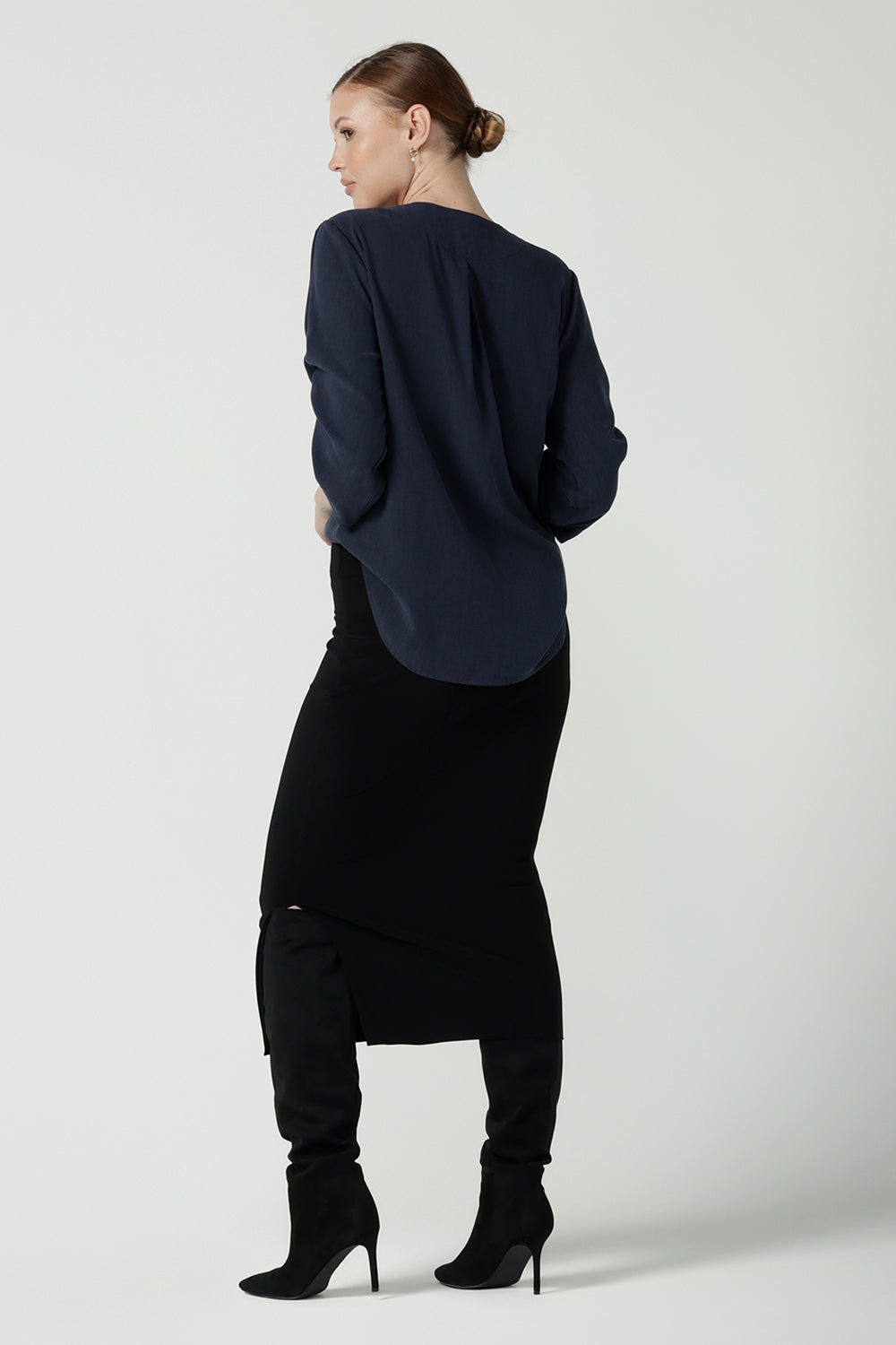 Back view of a a size 10 woman wears the Terry Top in Bluestone, a Navy tencel shirt that is breathable and soft. Made in high quality fabric in Australia. Soft V-neckline and ruched sleeves. Made in Australia for women size 8-24. Styled back with the Andi Midi tube skirt in black.