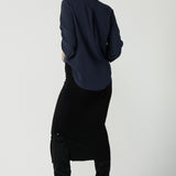 Back view of a a size 10 woman wears the Terry Top in Bluestone, a Navy tencel shirt that is breathable and soft. Made in high quality fabric in Australia. Soft V-neckline and ruched sleeves. Made in Australia for women size 8-24. Styled back with the Andi Midi tube skirt in black.