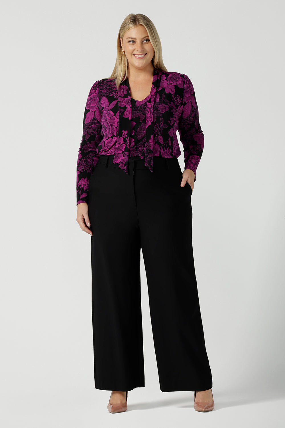 A size 18 model wears the Thom top in Fuchsia Flora is sophisticated and so versatile. Tie the neck-ties to the front for a day in the office or leave the ties open for your next event. Made in Australia for women size 8 - 24. Styled back with a Kade pant in black. 