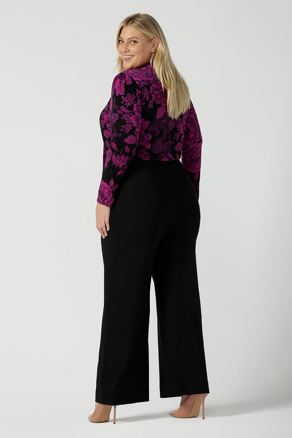 Back view of a size 18 model wears the Thom top in Fuchsia Flora is sophisticated and so versatile. Tie the neck-ties to the front for a day in the office or leave the ties open for your next event. Made in Australia for women size 8 - 24. Styled back with a Kade pant in black.