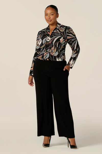A size 18, plus size woman wears a long sleeve, V-neck top with neck ties together with wide leg black work trousers. In black based, floral print jersey, this is an elegant work top and is a great top for plus size women with style! Shop made in Australia tops by women's clothing brand, Leina & Fleur.