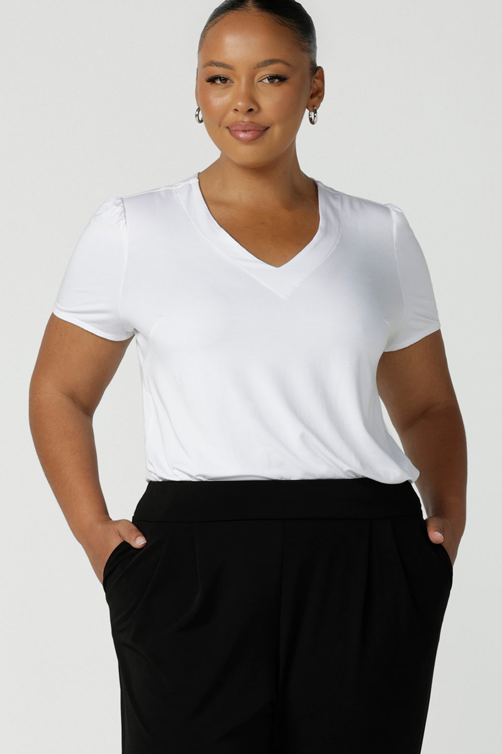 A size 18, plus size woman wears a V-neck, short sleeve top in white bamboo jersey. This tailored white top cuts a T-shirt look for casual wear and comfortable curve workwear. Shop made-in-Australia bamboo jersey tops online in petite, mid size and plus sizes at women's clothing brand, Leina & Fleur.