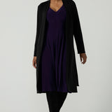 A size 10 woman wears a Amethyst purple Tracey dress in comfortable jersey. A great work wear style that is easy care with an empire line and 3/4 sleeves. Below knee length with a v-neckline. Petite to plus size size 8-24.Styled back with a Black Sorel trenchcoat and black boots. 