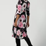 Back view of a size 10 woman wears the Tracey Dress in Night bloom. A Empire Line Dress with a floral print on a black base. Comfortable jersey design. Made in Australia for women size 8-24. Petite to plus size women.