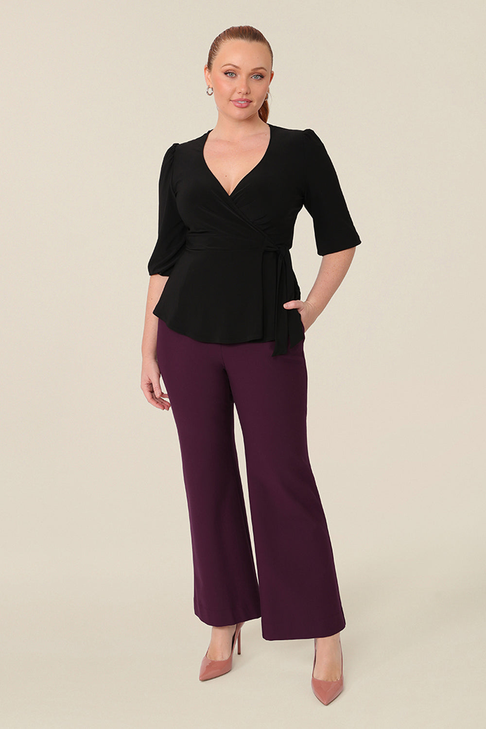 A size 12 woman wears a good top for curvy women. The Tristan Top is a functioning wrap peplum top and is worn with the Brett Pant in Mulberry. Both women’s top and pant are made in Australia in sizes 8 to 24.