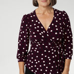 Mature aged model wears women's workwear top with flattering peplum silhouette. Its hemline dips gracefully at the back, offering extra coverage and a feminine touch. Available in sizes 8-24. Australian made from dry touch jersey fabric. 