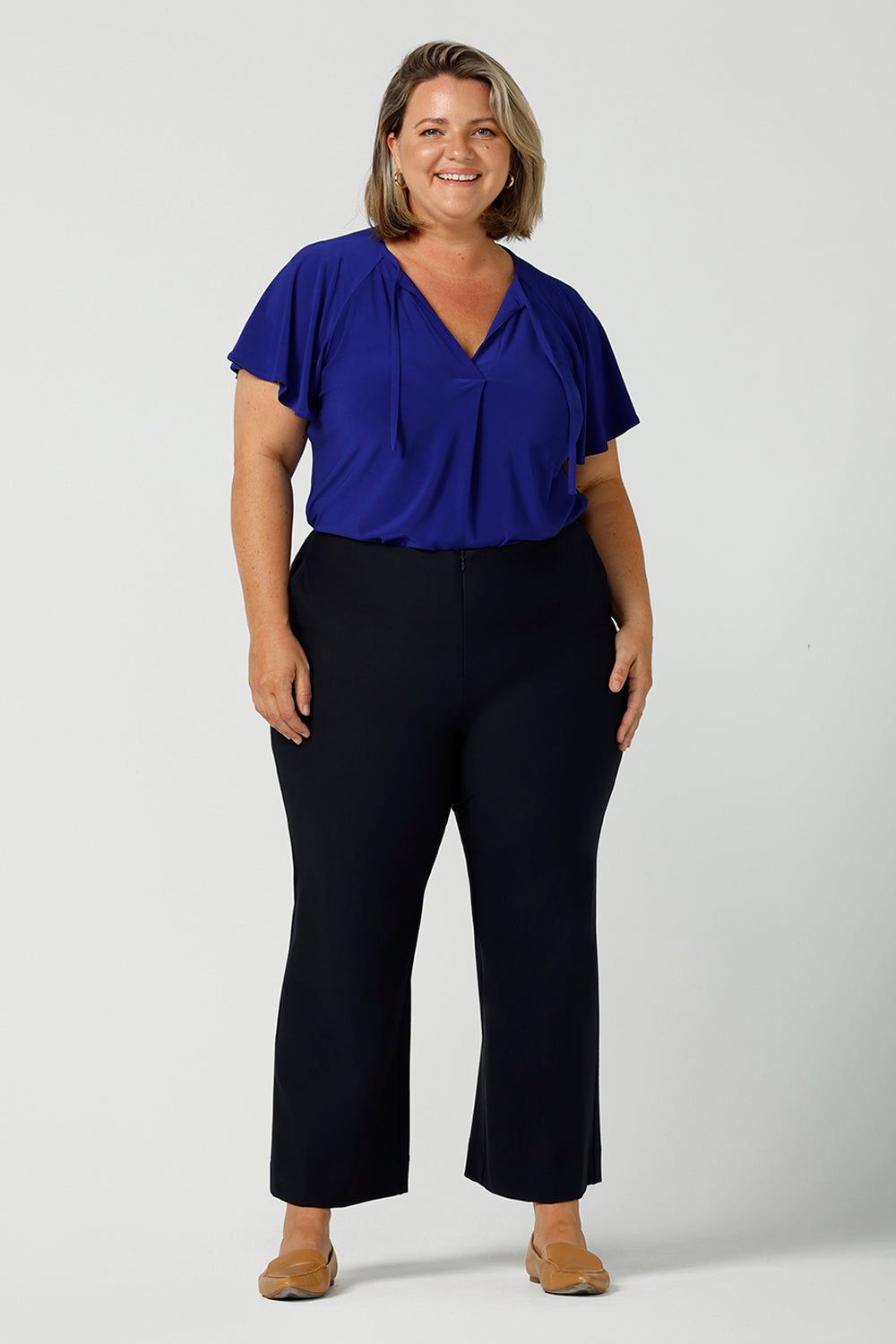 Great pants for curvy women, these flared leg, cropped pants are tailored for smart casual office wear. Worn with a V-neck, flutter sleeve top in cobalt blue, and shown on a size 18 woman, these plus size navy blue pants are made in Australia by Australian and New Zealand women's clothing brand, Leina & Fleur. Shop quality pants in sizes 8 to 24 in their online fashion boutique!