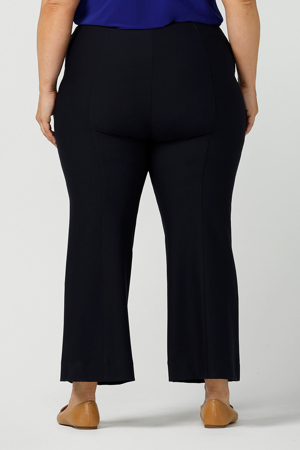 Back view of good pants for curvy women. These flared leg, cropped pants are tailored with back leg seams for smart casual office wear. Worn with a V-neck, flutter sleeve top in cobalt blue, and shown on a size 18 woman, these plus size navy blue pants are made in Australia by Australian and New Zealand women's clothing brand, Leina & Fleur. Shop quality pants in sizes 8 to 24 in their online fashion boutique!