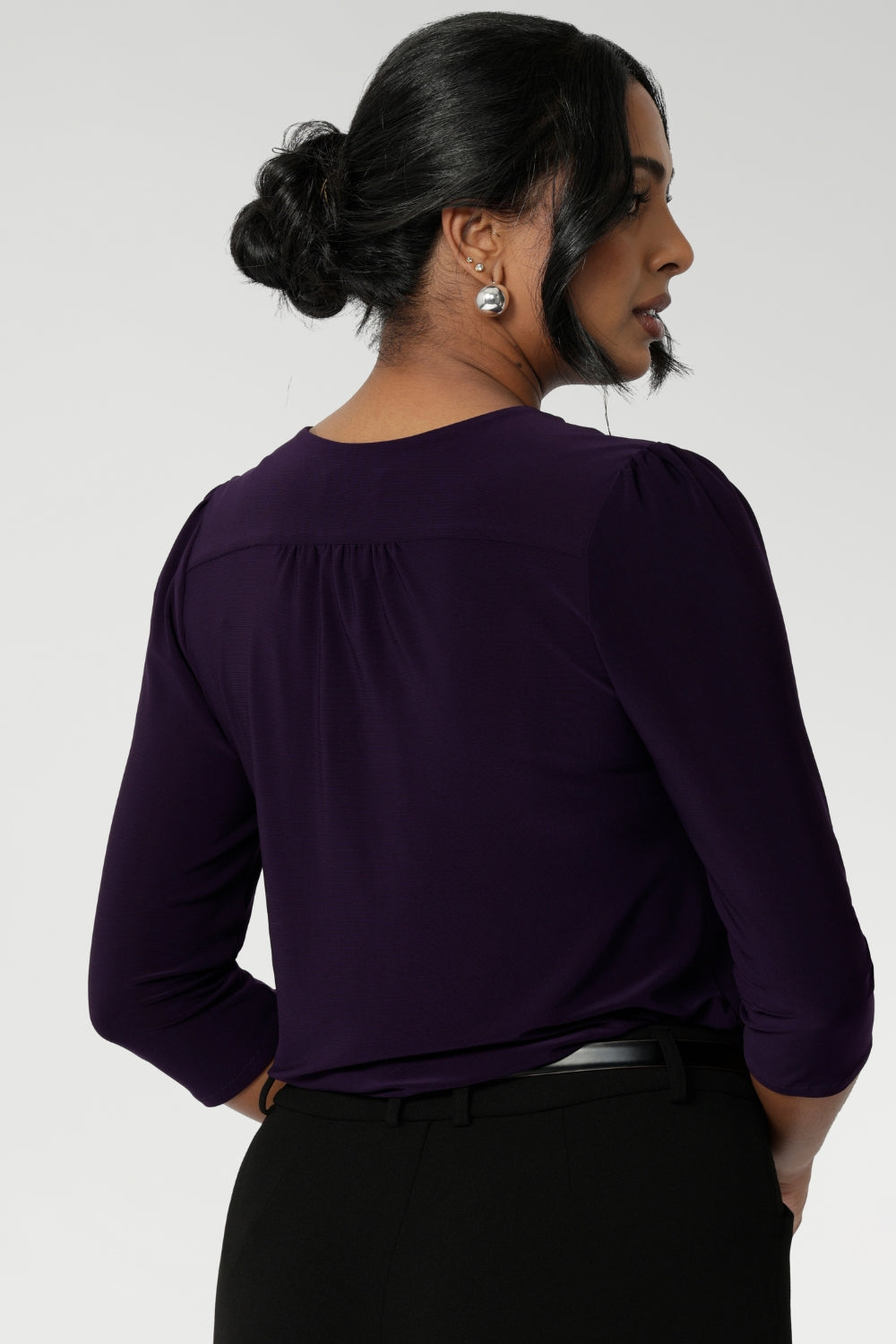 Close up image of Amethyst coloured woman's workwear shirt displays the tailored details such as centre-back gathers and shoulder tucks. Size 10 woman workwear shirt is worn tucked into black tailored pants with belt loops.