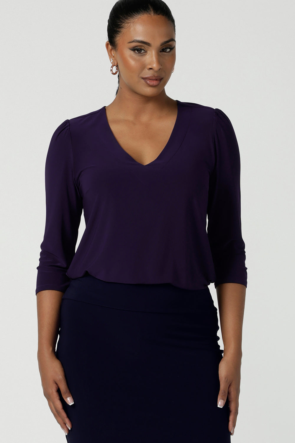 A size 10 woman wears the Vida Top in a size 10. A purple amethyst top with v-neckline and 3/4 sleeves. Styled back with an Andi Midi Tube skirt in Navy. Made in Australia and size inclusive fashion label petite to plus size 8-24. 