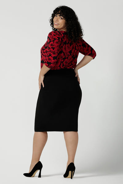 Back view of a Vida Top with a v-neck and bold poppy floral. Comfortable workwear top for women size 8 - 24. Black base with a red flower. Versatile and comfortable workwear. Styled back with a black slim Andi tube skirt. Made in Australia for women size 8 - 24.