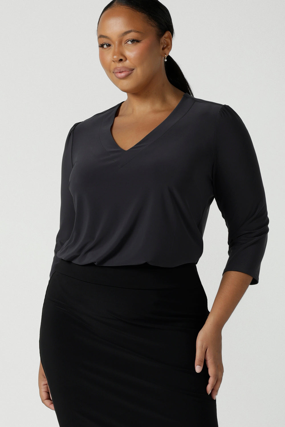 Size 16 woman wears the Vida top in Charcoal, a grey work top for women with a V-neckline. Comfortable corporate workwear for women. Made in Australia for women. Size 8 - 24.