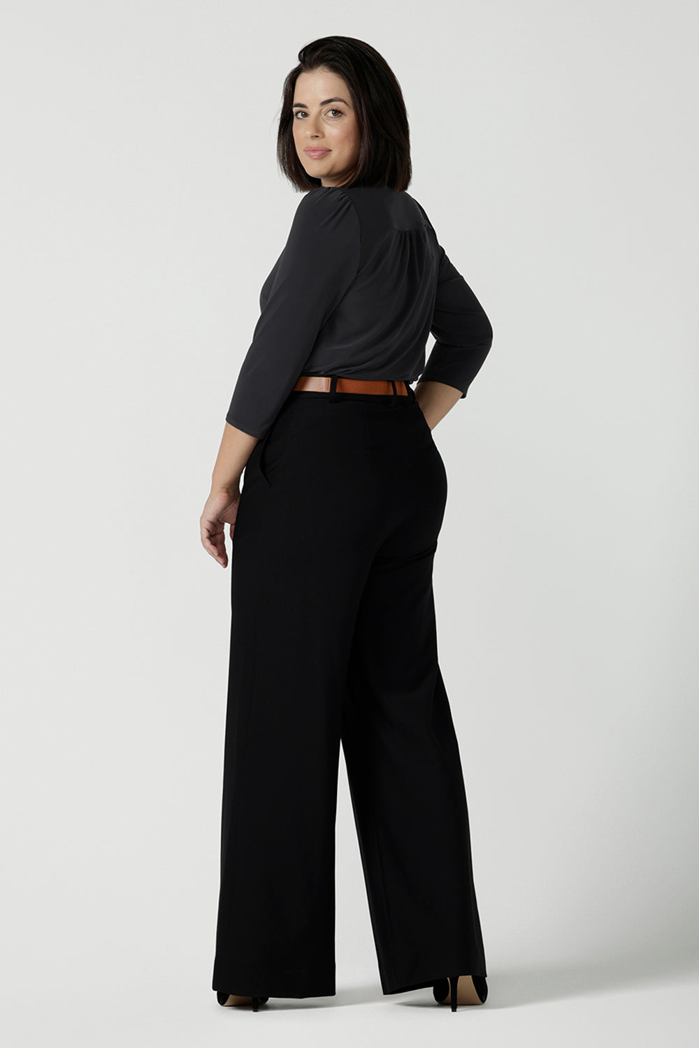 Back view of size 10 woman wears the Kade pant in black, a softly tailored black pant in ponte jersey. Functioning fly front, belt loops, side pockets and a straight let. Made in Australia for women size 8 - 14. Styled back with the Vida top in charcoal 3/4 sleeves and a v-neckline.