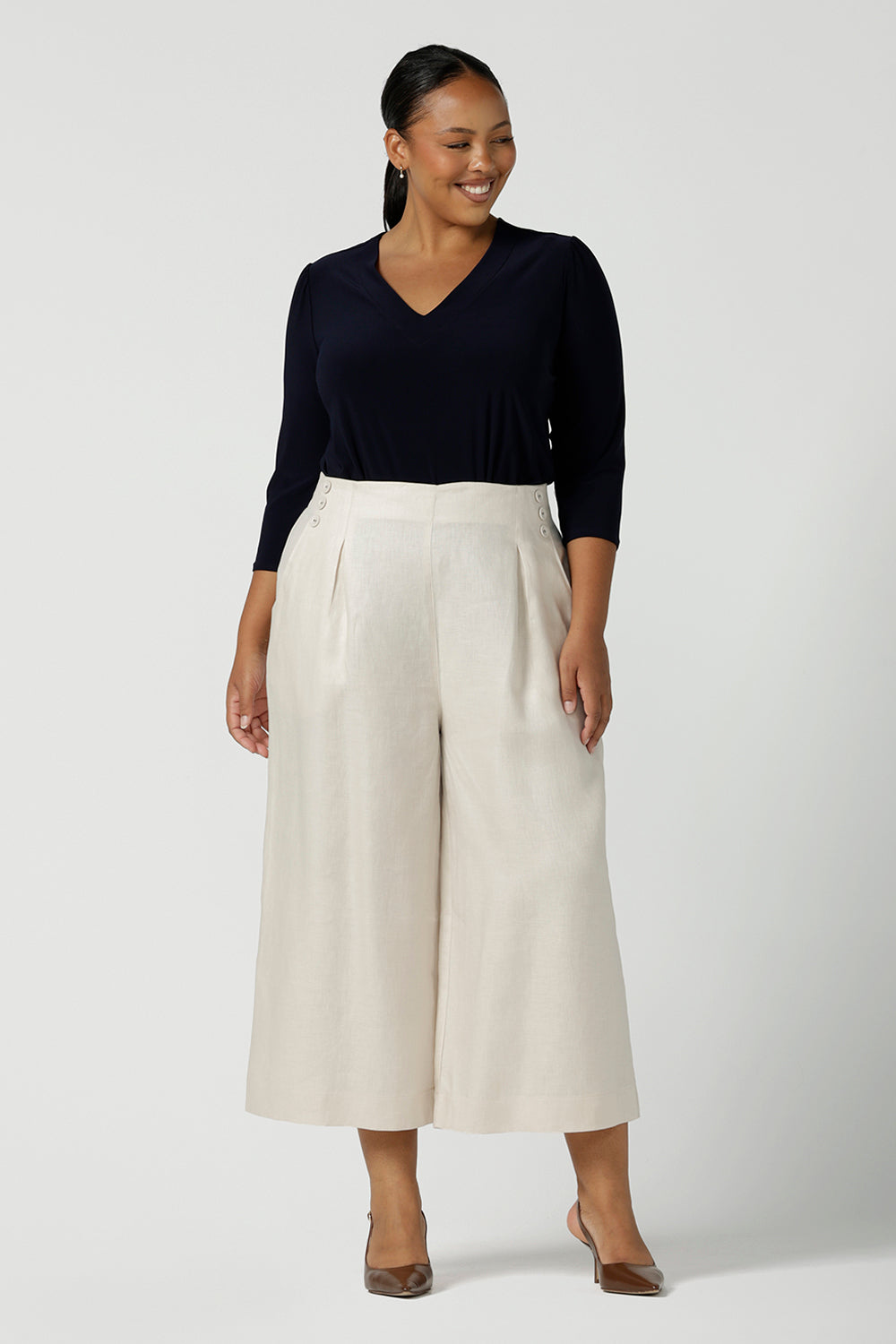 A curvy size 16 woman wears a vida top in Navy with a V-neckline and 3/4 sleeves. Made in comfortable jersey for corporate workwear to casual wear. Styled back with Nik Pant in parchment linen, a wide leg culotte. Made in Australia for women size 8 - 24. 
