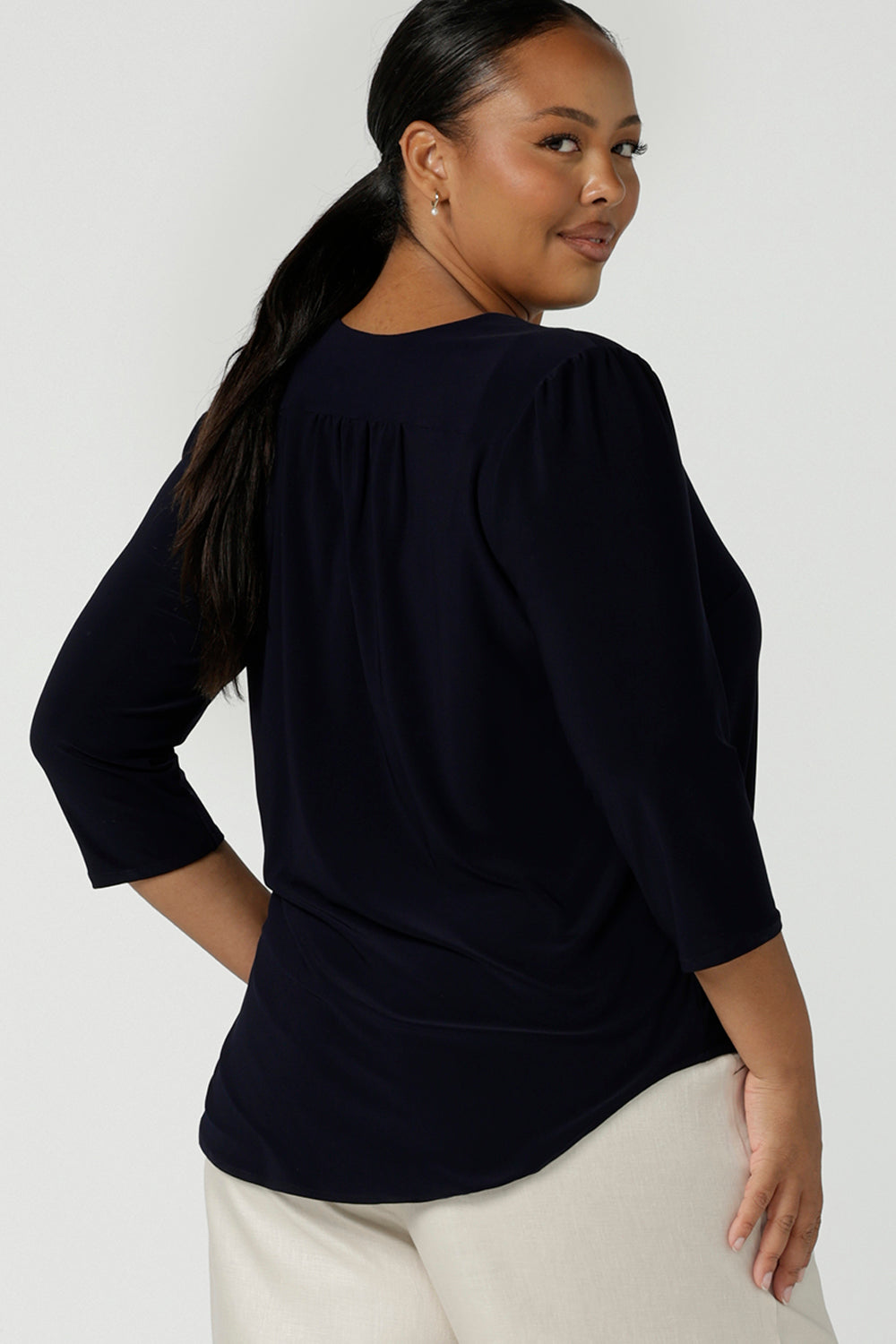 Back view of a curvy size 16 woman wears a vida top in Navy with a V-neckline and 3/4 sleeves. Made in comfortable jersey for corporate workwear to casual wear. Made in Australia for women size 8 - 24.