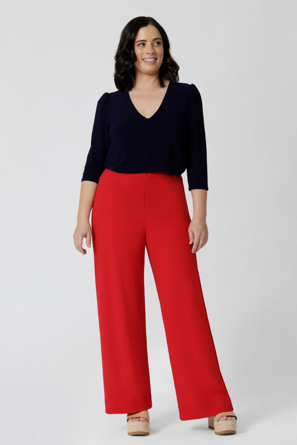 A petite size 10 woman wears a vida top in Navy with a V-neckline and 3/4 sleeves. Made in comfortable jersey for corporate workwear to casual wear. Styled back with soft suiting. Made in Australia for women size 8 - 24. 