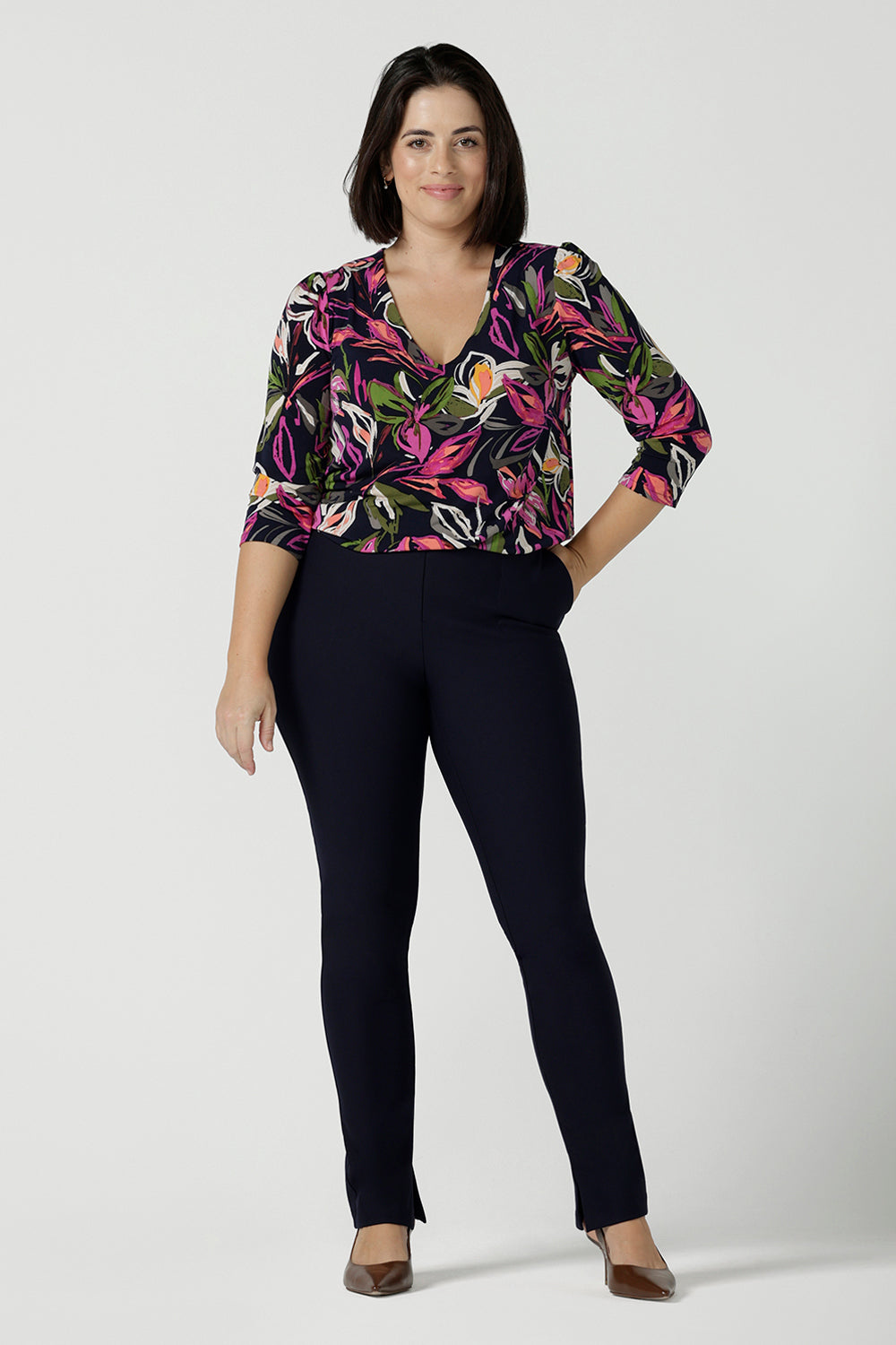 A size 10 woman wears the Vida top in Vivid Flora. A v-neckline style with 3/4 sleeves. Corporate casual work tops. Styled back with the Berit skirt in Charcoal. Made in Australia for women size 8 - 24.
