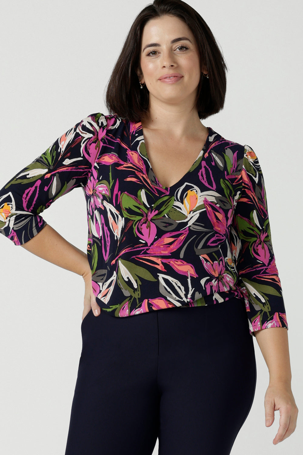 Close up of a size 10 woman wears the Vida top in Vivid Flora. A v-neckline style with 3/4 sleeves. Corporate casual work tops. Styled back with the Berit skirt in Charcoal. Made in Australia for women size 8 - 24.
