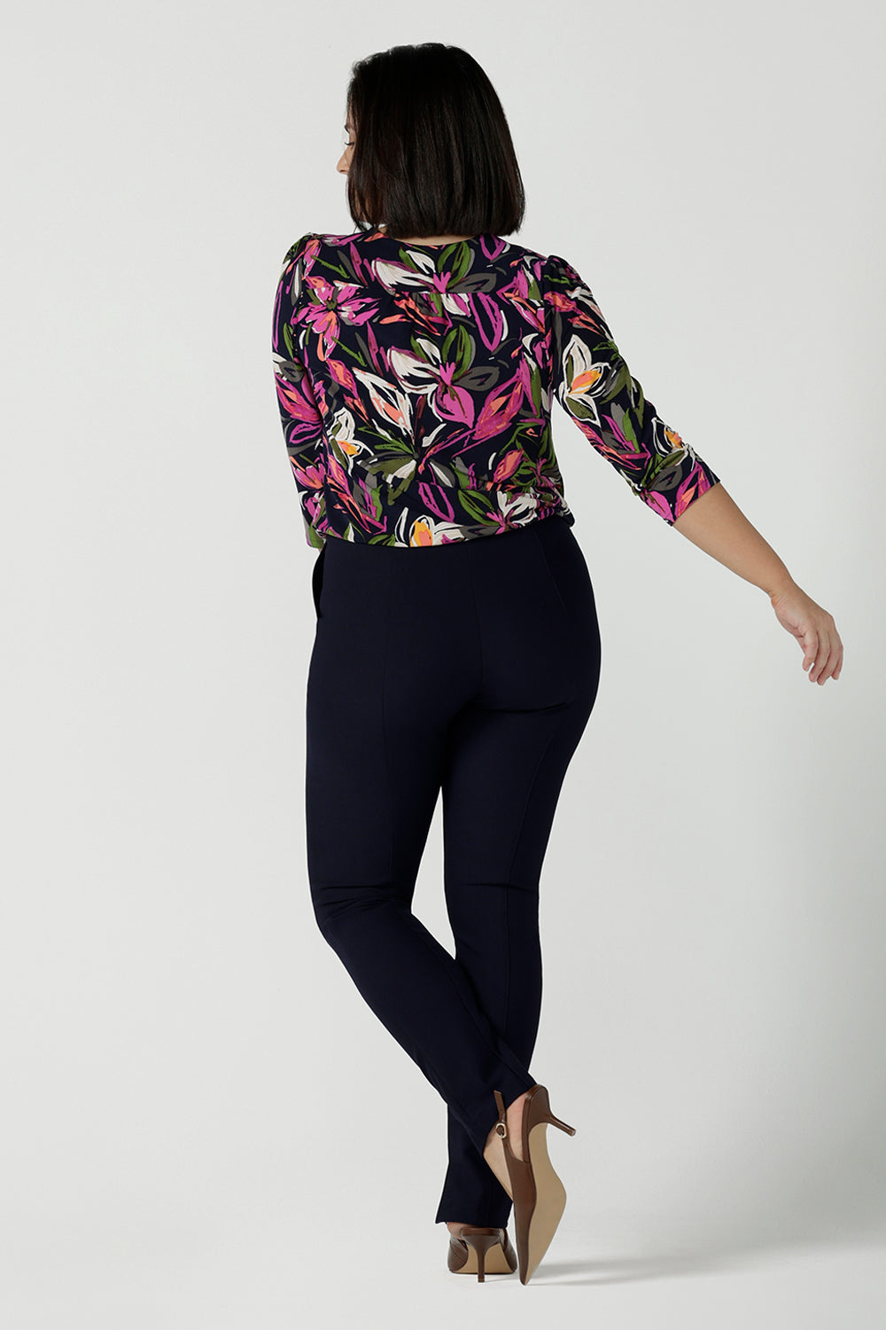 Back view of a size 10 woman wears the Vida top in Vivid Flora. A v-neckline style with 3/4 sleeves. Corporate casual work tops. Styled back with the Berit skirt in Charcoal. Made in Australia for women size 8 - 24.