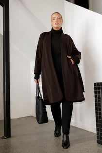 The Sorel Trench Coat is expertly tailored with a modern, sophisticated silhouette that elevates any wardrobe. Size 18 woman wears winter coat crafted from a luxurious winter-weight Modal fabric over long length black pants, black turtle neck, and high heel boots for an elevated workwear look. 