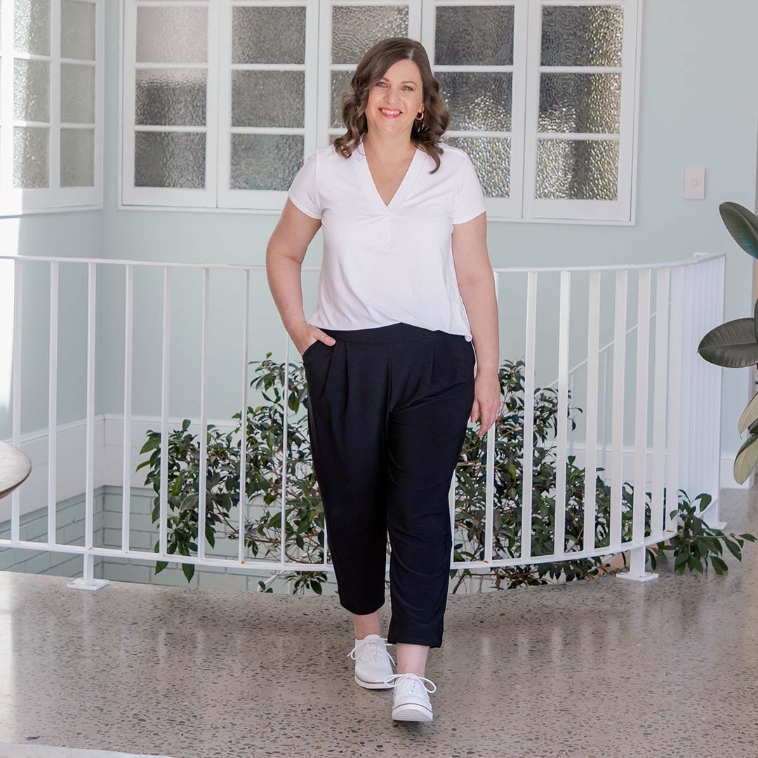 Showing pant styles for petite women, a curvy woman wears black jersey pants with tapered, cropped legs. Worn with a short sleeve white bamboo jersey T-shirt top, these casual trousers are great for casual wear and also make comfortable travel pants for women of all sizes thanks to Leina & Fleur's 8 to 24 size range.