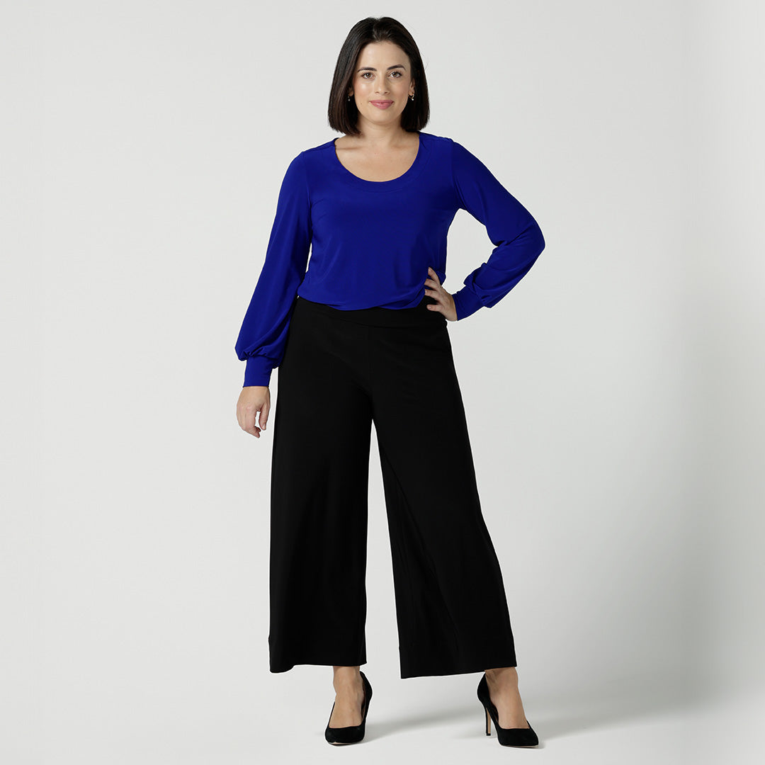 Showing great pants for petite height women, a petite woman wears wide leg culotte pants in black with a cobalt blue, long sleeve, round neck top. Both top and wide leg trousers are made in Australia by Australian and New Zealand women's clothes brand, Leina and Fleur. 