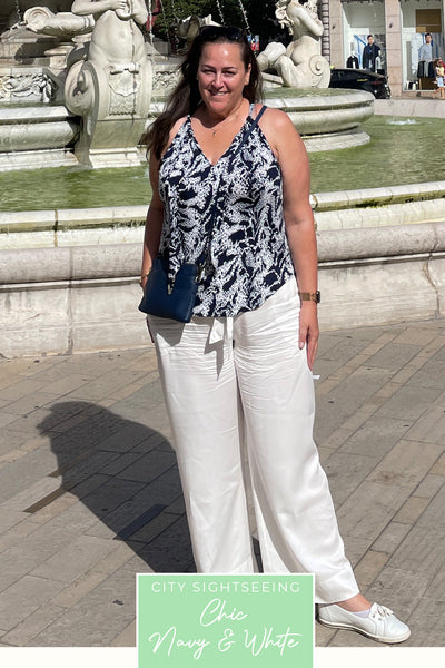 A plus size, curvy woman wears a navy and white print jersey top and wide leg white pants in sustainable Tencel fabric as part of her travel capsule wardrobe for a holiday in France.