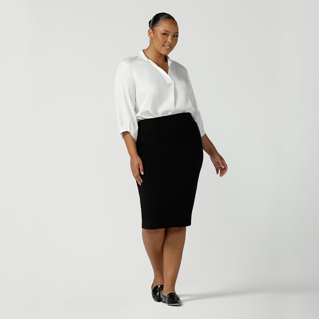 A great tube skirt for workwear, a curvy, size 18 woman wears a knee-length black tube skirt with a white pull on shirt.