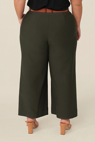 Back view of good pants for petite women, these are wide leg, cropped, tailored workwear pants. Worn by a petite height, size 16 curvy woman, together with a short sleeve, black top and tan belt. Made in Australia, in stretch jersey, these work trousers have a comfortable fit.