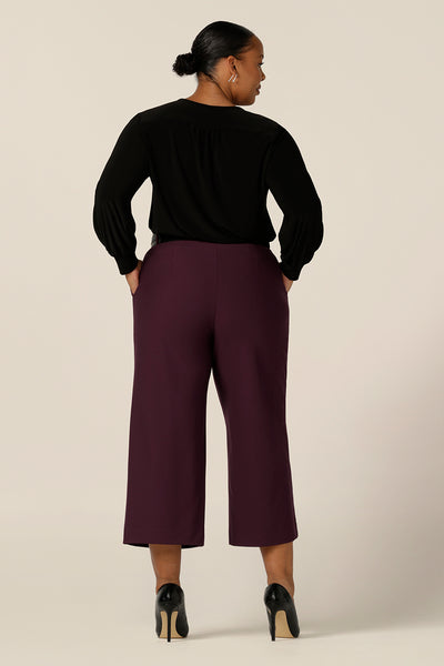 Back view of a size 18, curvy woman wearing wide leg, cropped length, tailored pants in Mulberry ponte jersey with a long sleeve, V neck top in black jersey. Made in Australia by Australian and New Zealand women's clothing label, L&F, these easy care pants work for corporate wear and weekend wear