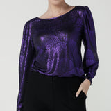 A size 10 woman wears the Zara top in purple metallic fabric. With balloon sleeves and a boat neckline. Styled back with black brooklyn ponte pants. The perfect cocktail suit set made in Australia for women size 8-24