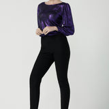 A size 10 woman wears the Zara top in purple metallic fabric. With balloon sleeves and a boat neckline. Styled back with black brooklyn ponte pants. The perfect cocktail suit set made in Australia for women size 8-24