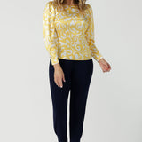 A size 10 woman wears a Zara Top in Yellow Swirl silk. A long sleeve blouse with fashion sleeve and made in 100% silk. Made in Australia for women size 8-24. Styled back with the Indi Tall Pant in Navy. 