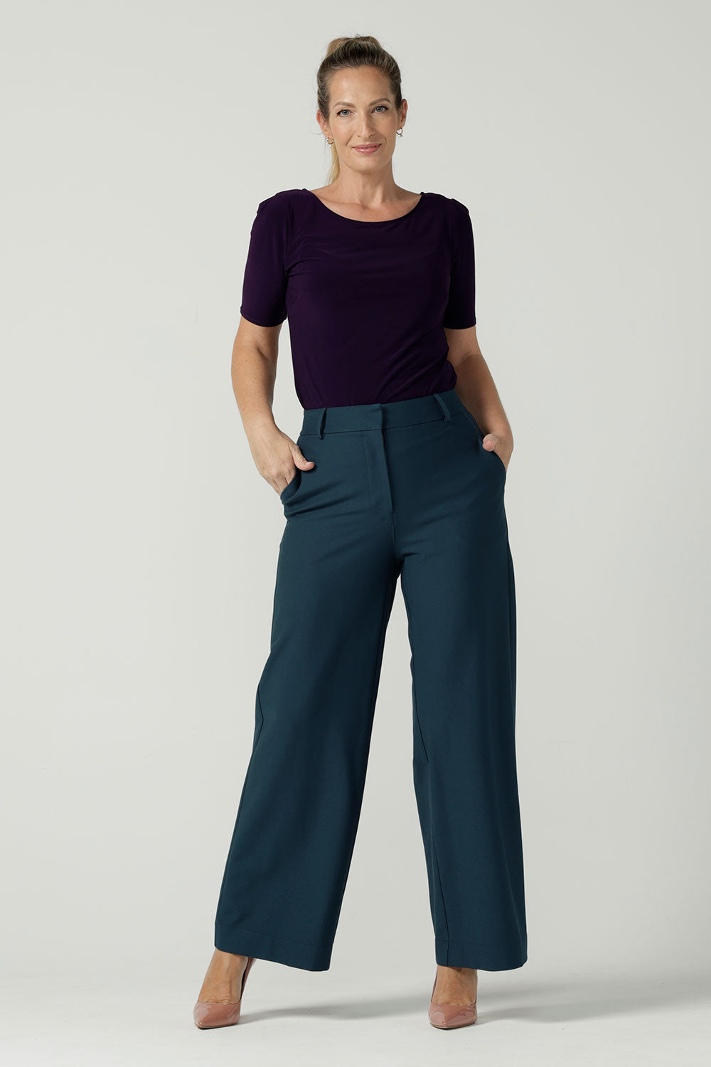 A Size 10 woman wears the Ziggy top in Amethyst, a boat neckline style with a pleat tuck on the sleeve head and slight curve hem. Made in Australia for women size 8 - 24.