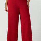 Close up of a size 16 woman wears the Drew pant in red, high waist and invisible fly front. Tailored belt loops and wide leg. Made in Australia for women. Stylish corporate wear for women. Made in Australia size 8 - 24.