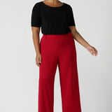 Size 16 woman wears the Drew pant in red, high waist and invisible fly front. Tailored belt loops and wide leg. Made in Australia for women. Stylish corporate wear for women. Made in Australia size 8 - 24. 