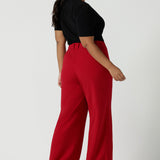 Back view of a size 16 woman wears the Drew pant in red, high waist and invisible fly front. Tailored belt loops and wide leg. Made in Australia for women. Stylish corporate wear for women. Made in Australia size 8 - 24.